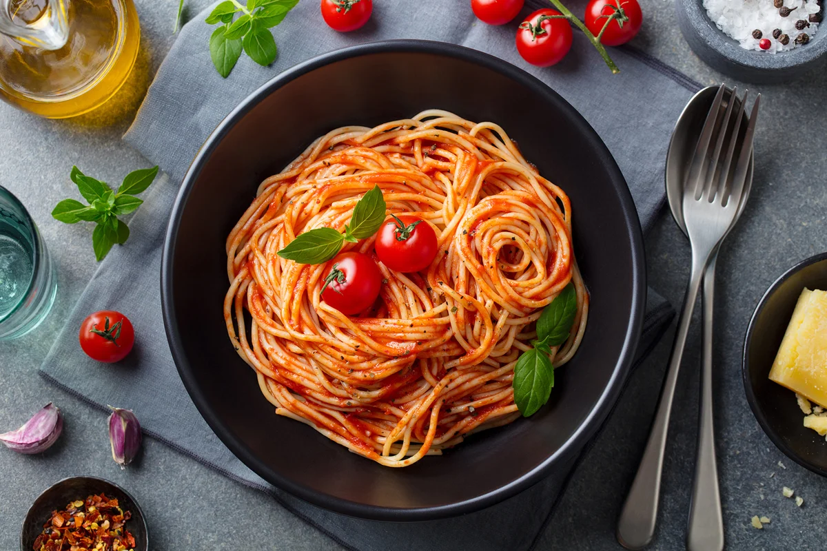 Pasta, spaghetti with tomato sauce in black bowl on grey stone background