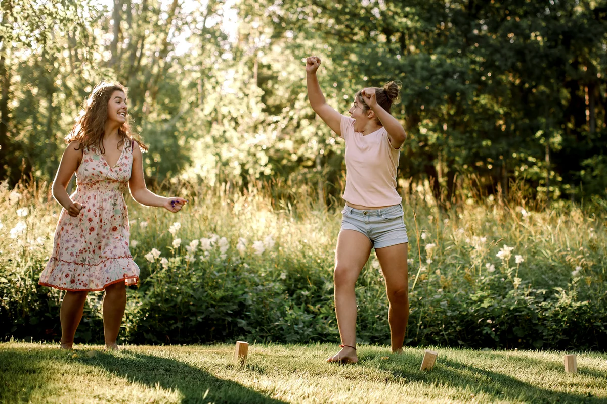 Happy siblings looking at each other while playing molkky in backyard