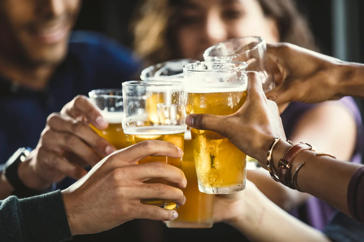 Group of friends toasting beer glasses at table in bar