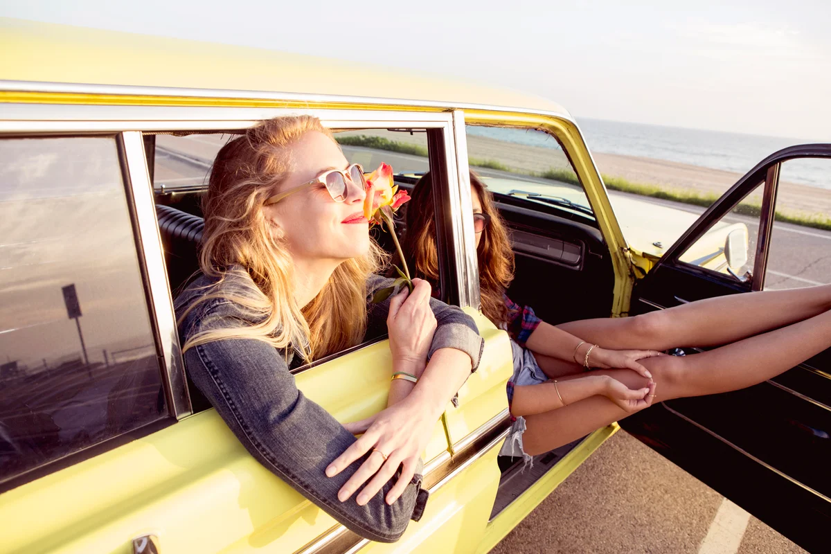 Young woman sitting in car with friend at beach