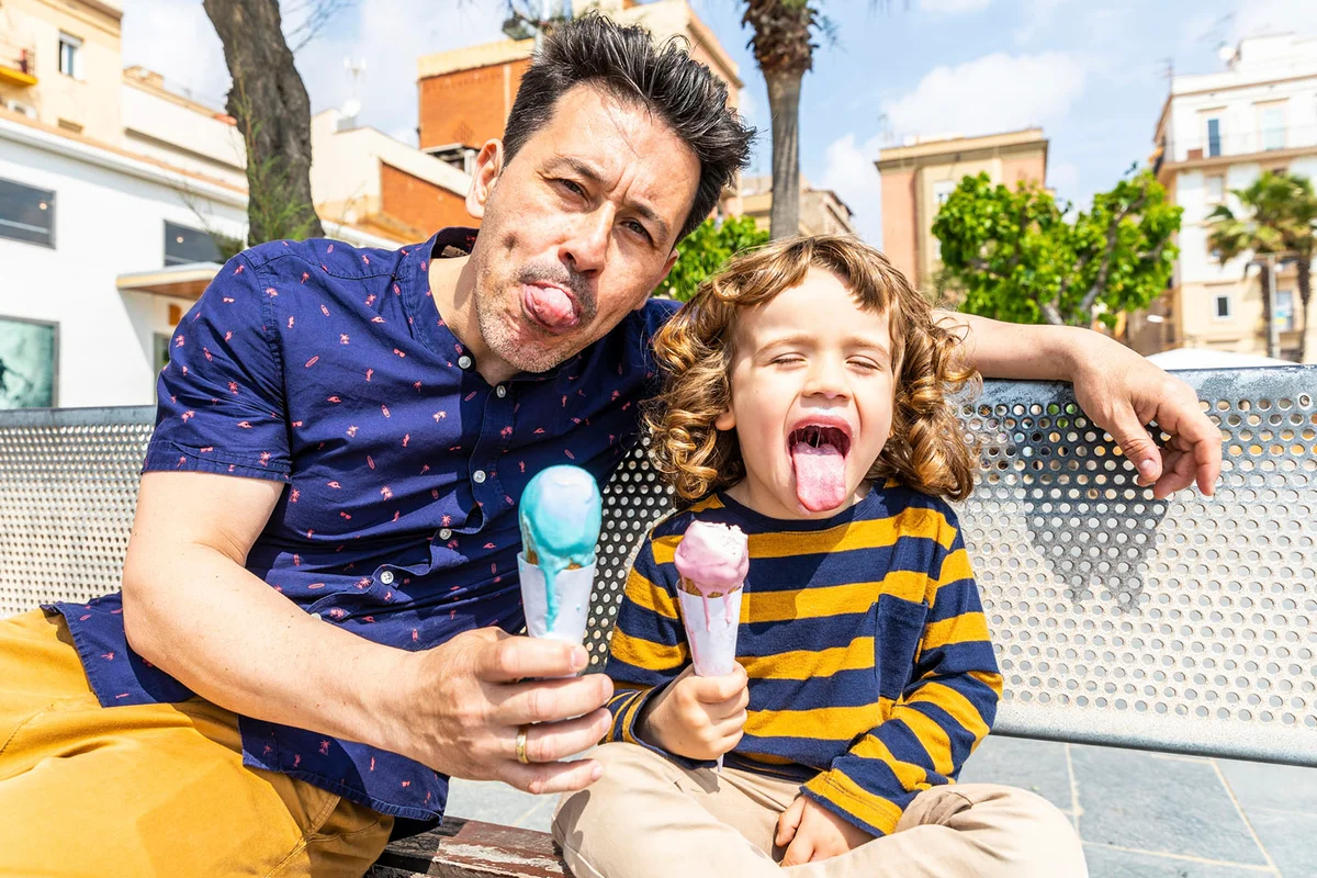 happy father and son sitting on bench enjoying an ice cream