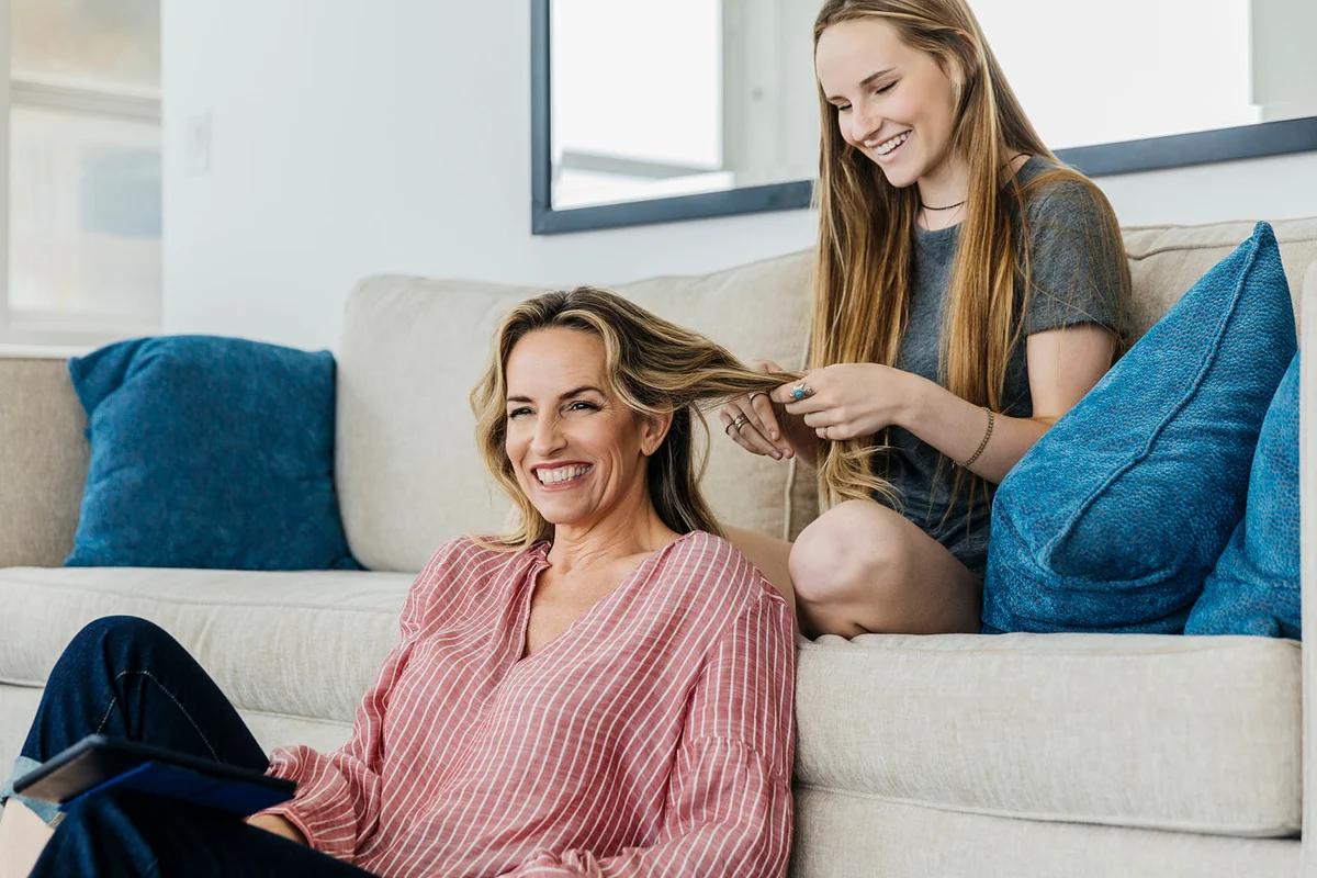 Smiling daughter playing with mother's hair while sitting at home