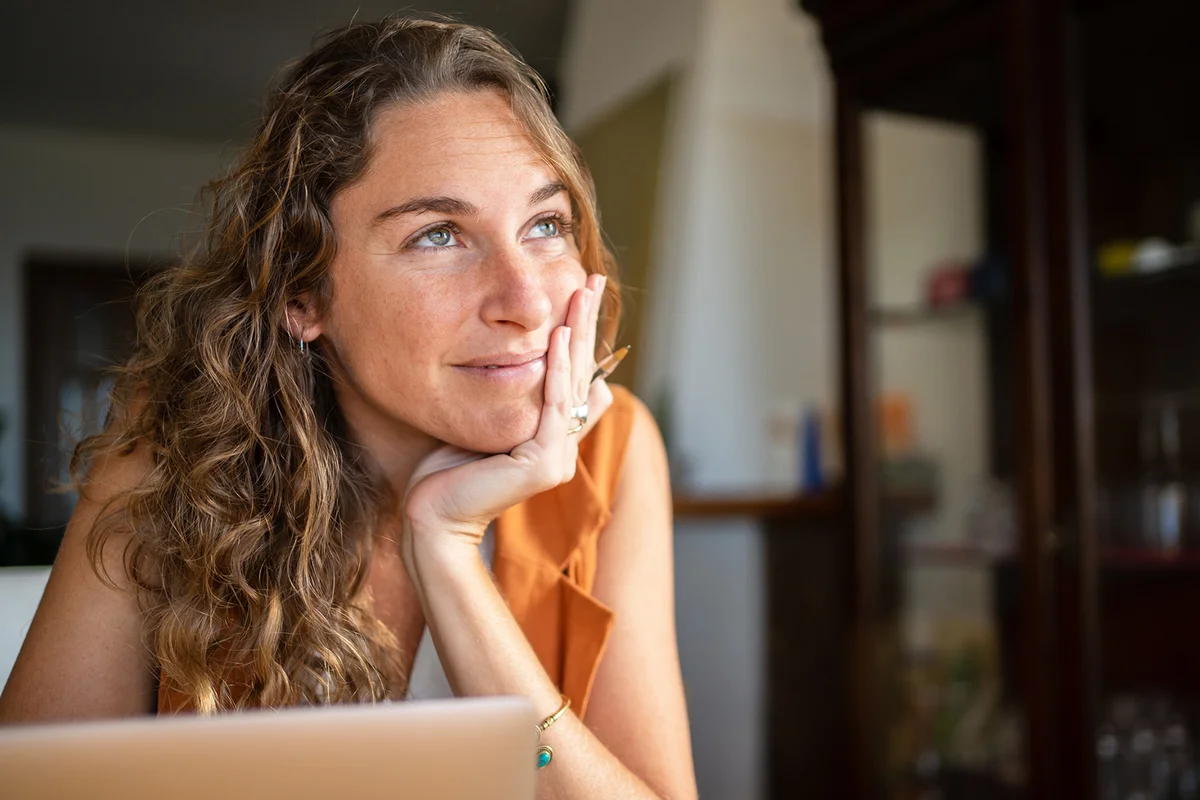 A woman with a dreamy expression working with a laptop from home