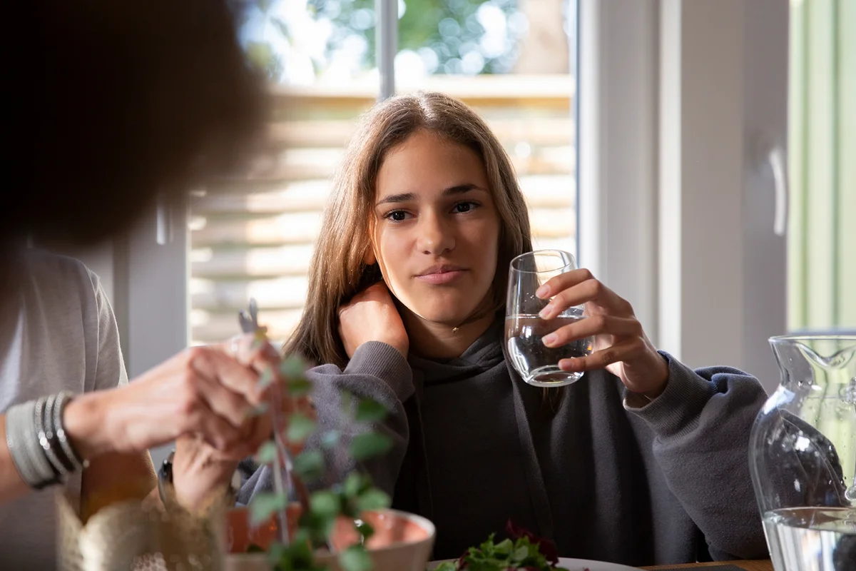 Girl holding drinking glass while having food with mother at home