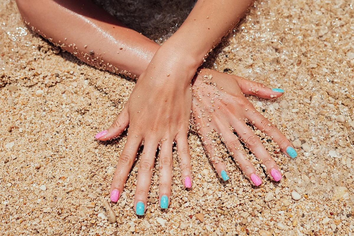 Beautiful female hands with pink and blue manicure nails on sea sand background