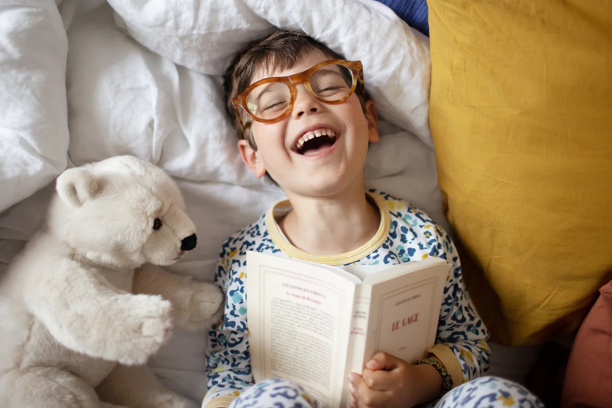 A 4 year old little boy having fun, laying on a bed