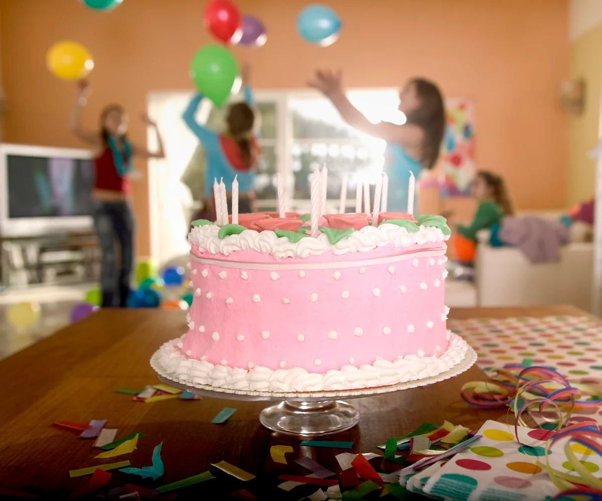 closeup of pink birthday cake with teens in the background