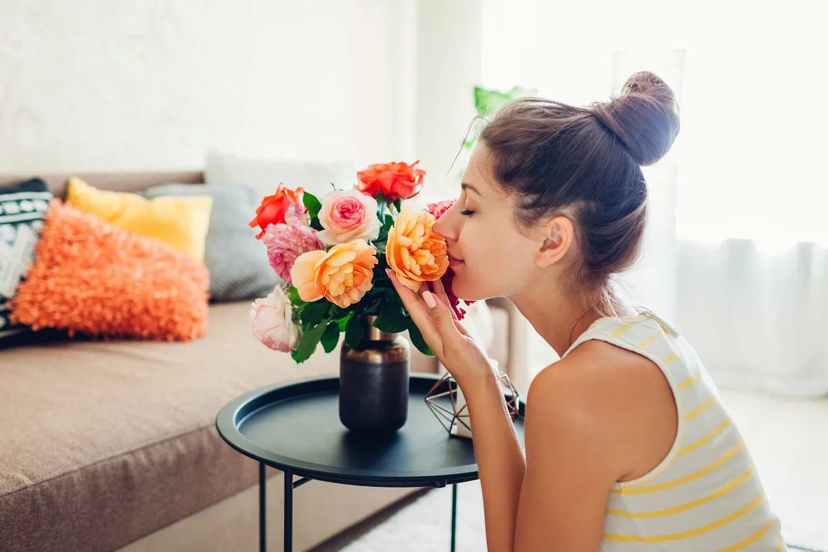 Woman smelling vase of colorful roses in her home