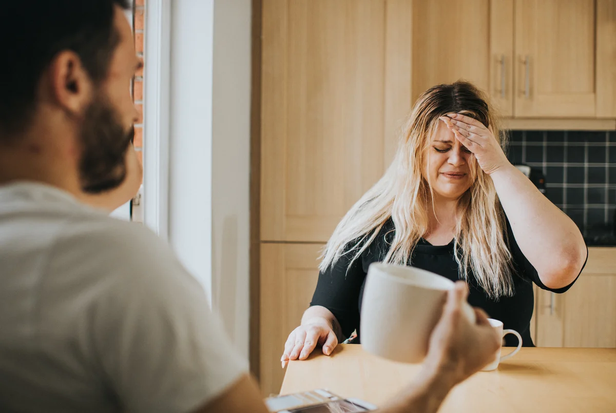 Man and woman sitting at table, woman is crying and distressed