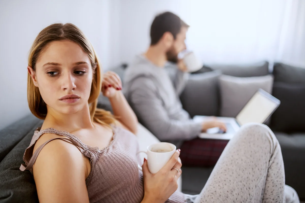 Man on laptop while woman looks away sadly