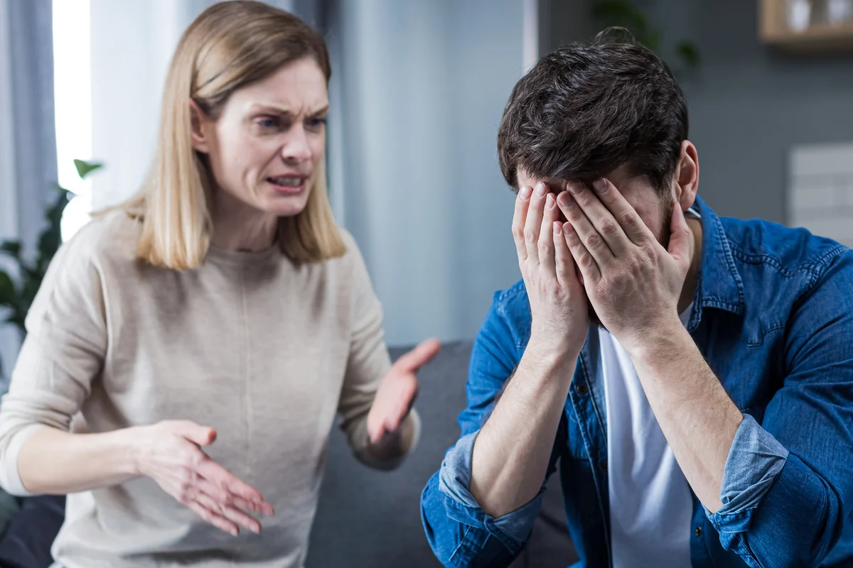 Woman angrily yelling at man while he covers his face