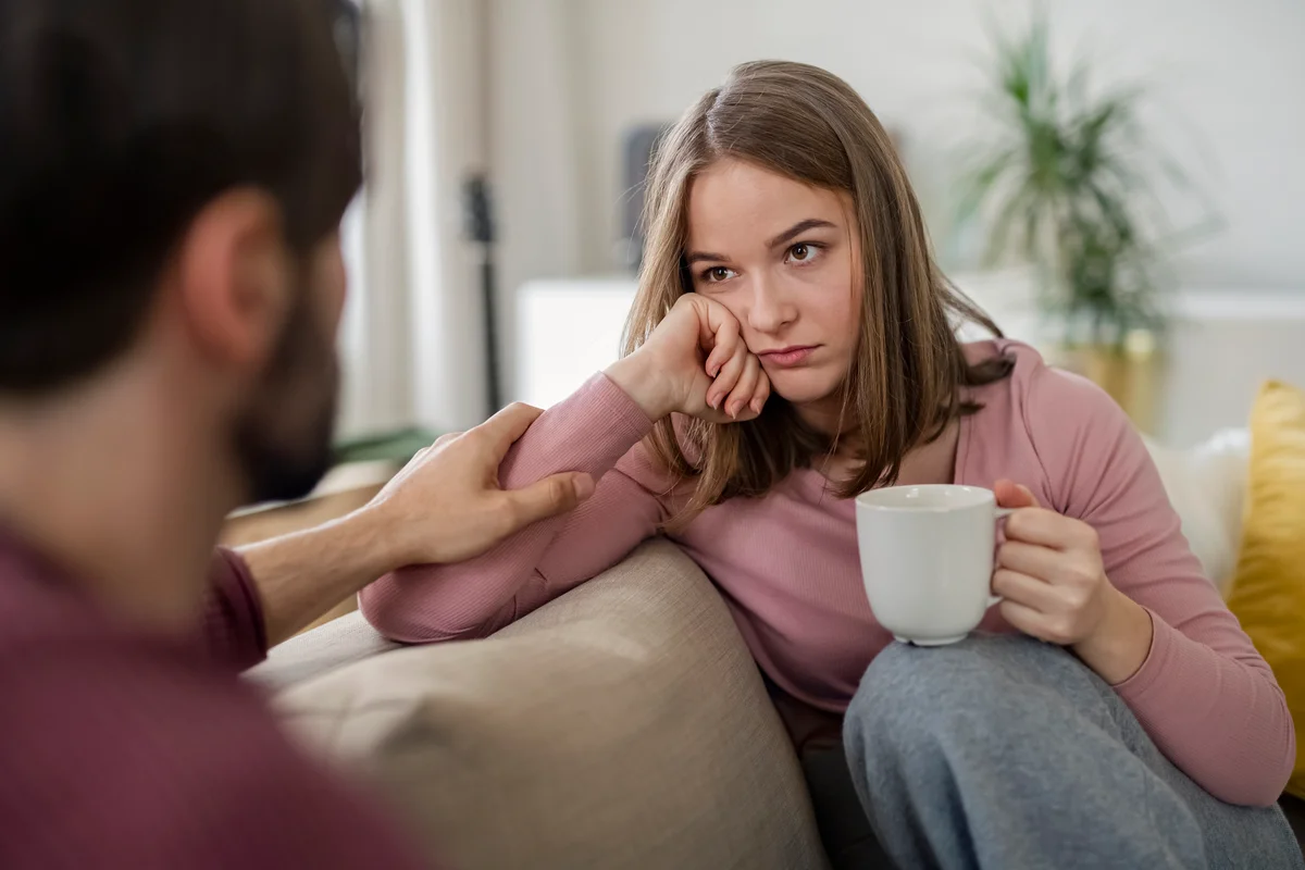 Woman looks unhappily at man while he puts his hand on her