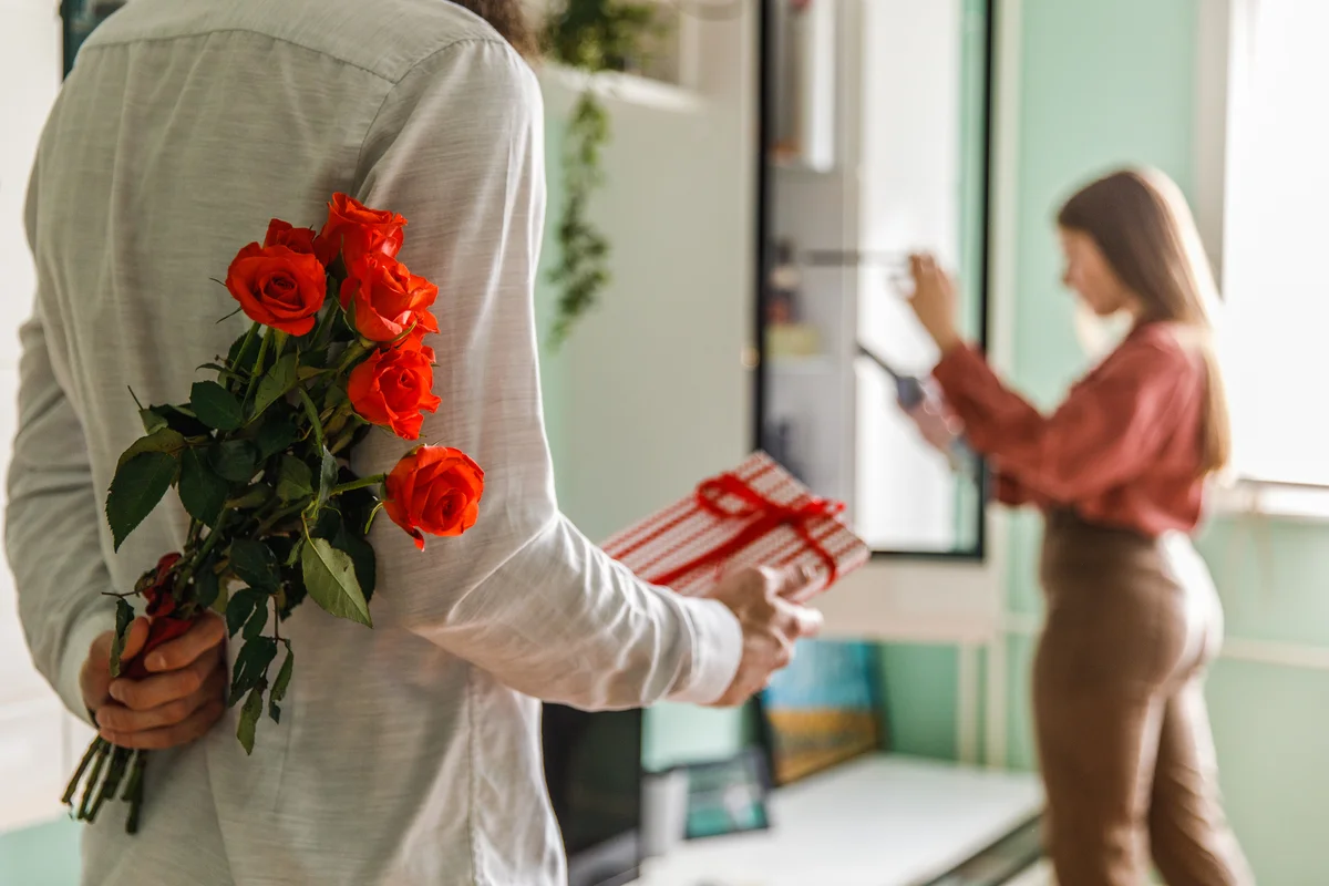 Man approaching woman to give her a gift and flowers