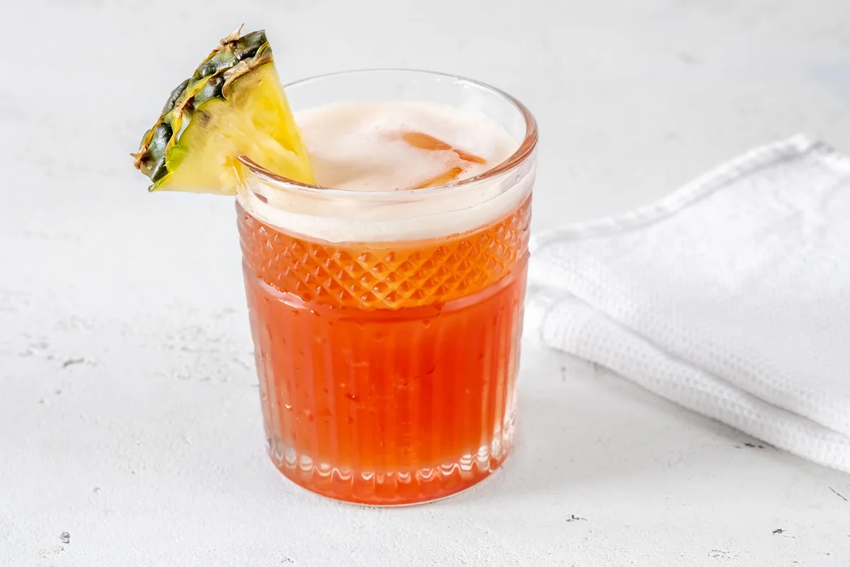 Glass of Jungle Bird cocktail garnished with pineapple wedge