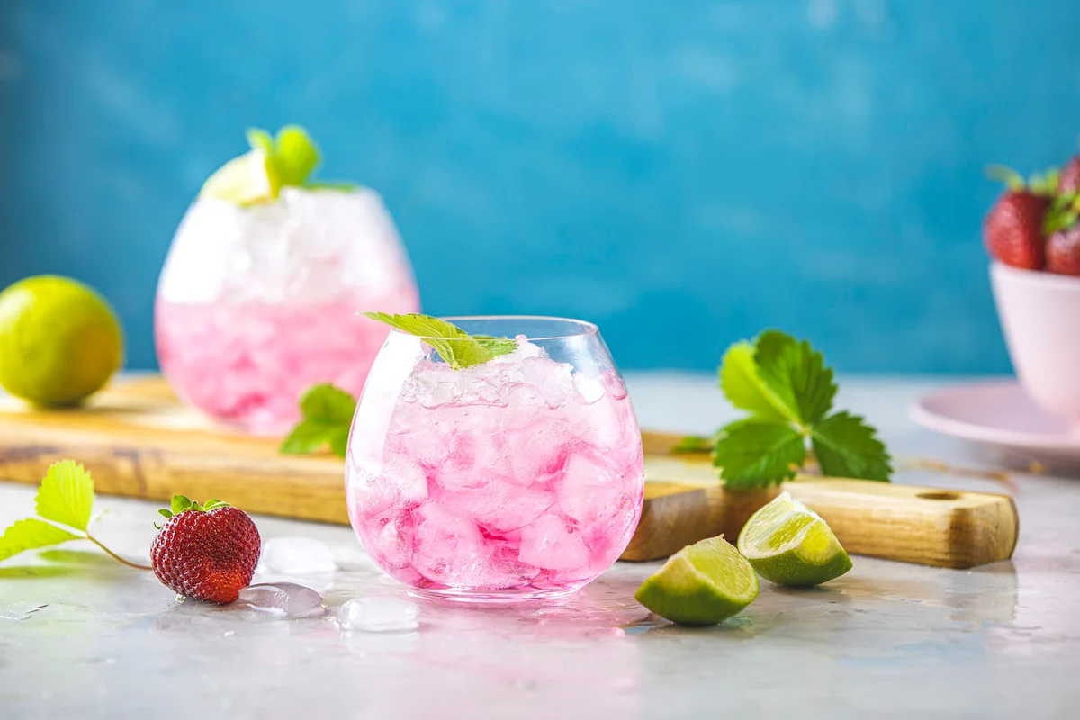 Pink cocktail with lime, crushed ice, strawberries and mint