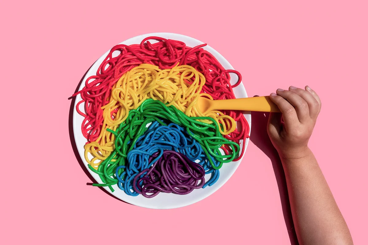 Hand of baby girl eating rainbow-colored spaghetti