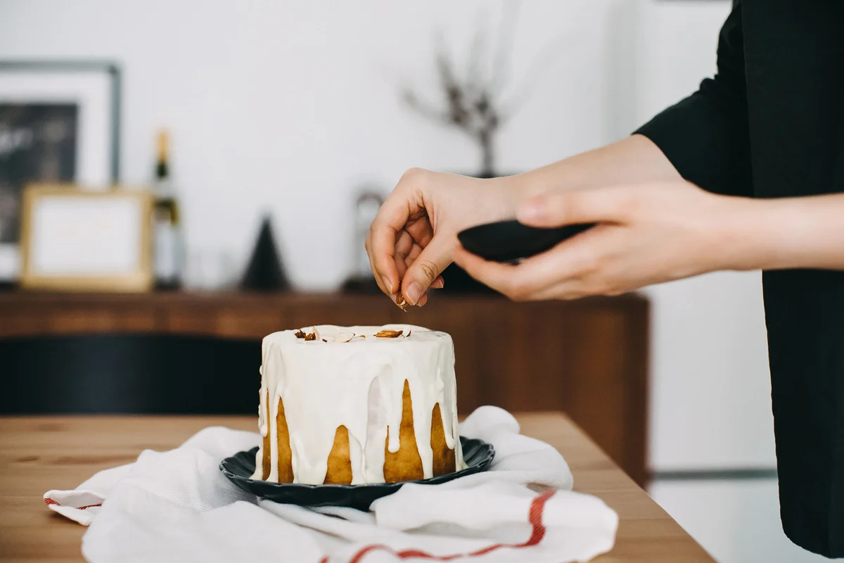 Woman decorating and sprinkling nuts on top of an iced cake
