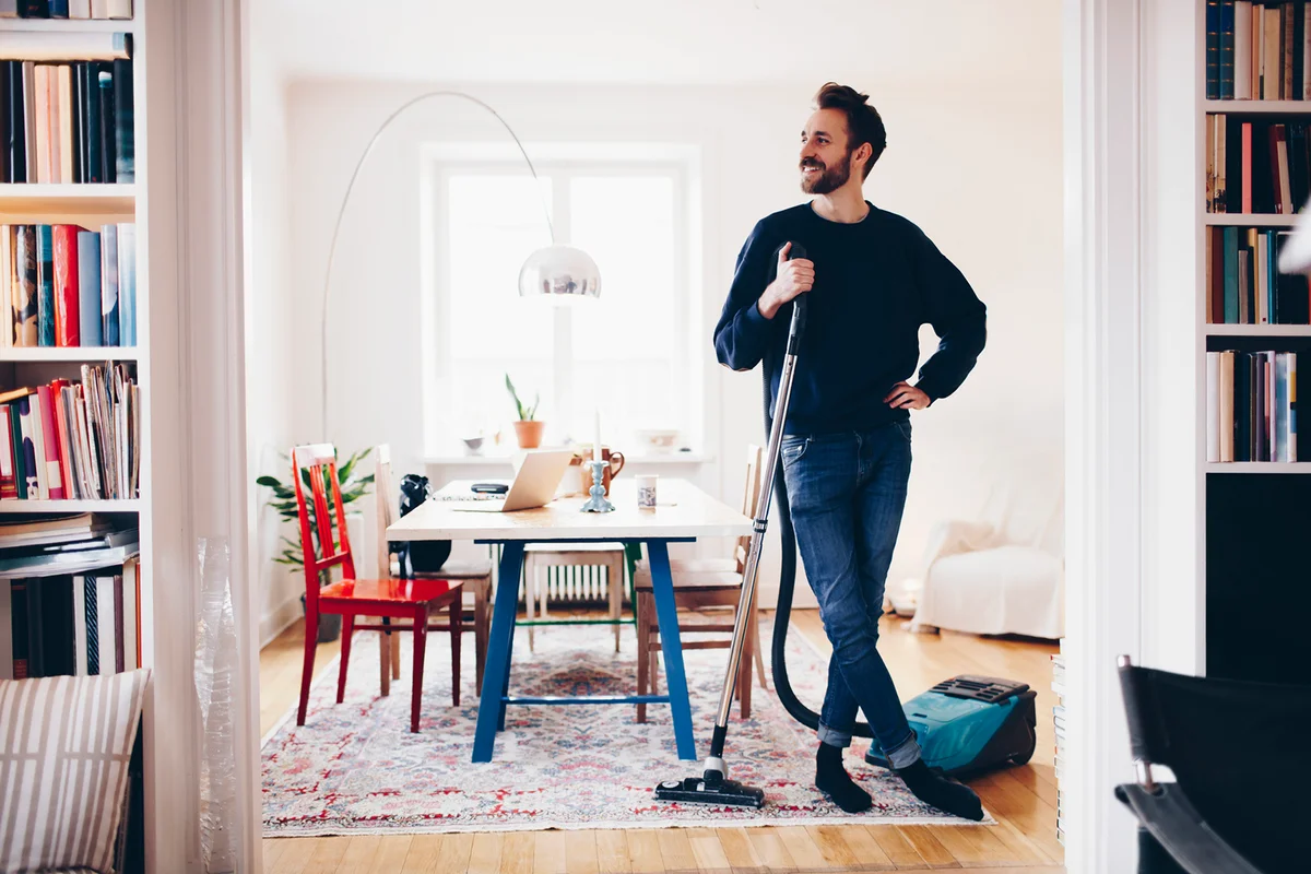 Happy man standing with vacuum cleaner in dining room at home