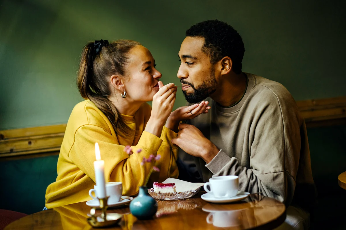Girlfriend feeding bite of dessert to her boyfriend at cafe