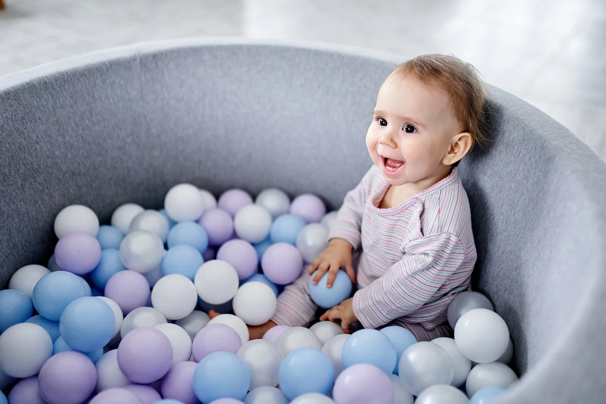 A baby girl is sitting in a pile of colorful balls of pastel colors