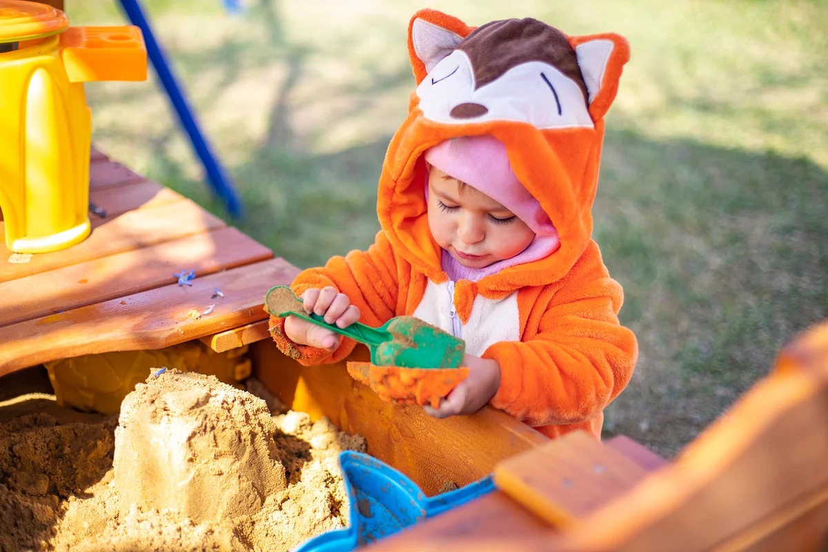 Cute toddler in orange jumpsuit plays in the sand