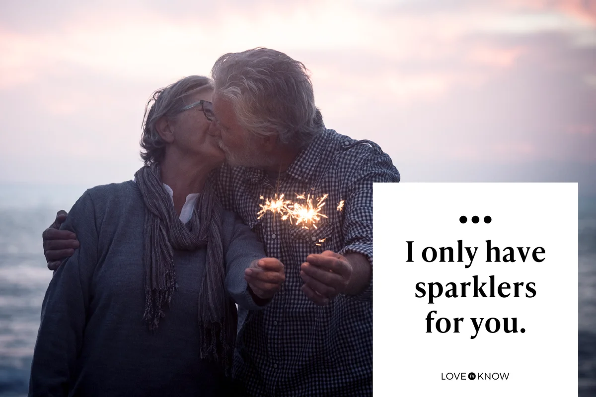 Kissing senior couple standing in front of the sea by sunset holding sparklers
