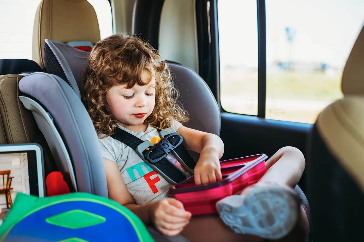 Young girl sitting in a car seat and eating lunch on a road trip