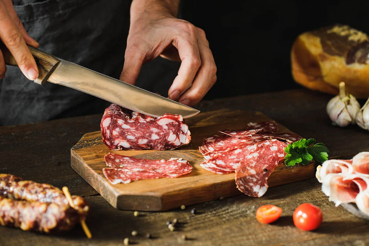 Woman hands cutting salami sausage on wooden board