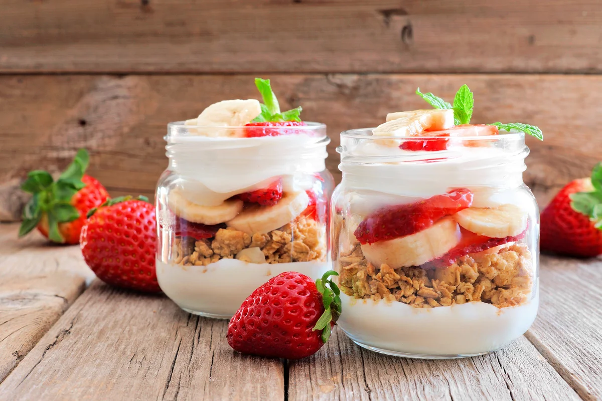 Strawberry and banana parfaits in mason jars over rustic wood