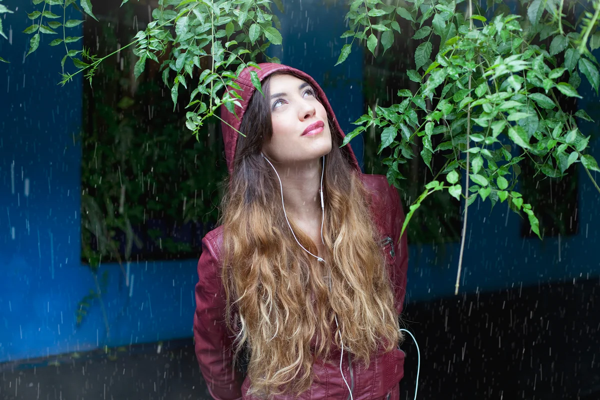 Young woman hiding from rain, listening to music