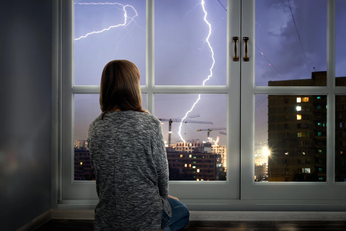 The girl looks through the window at the lightning