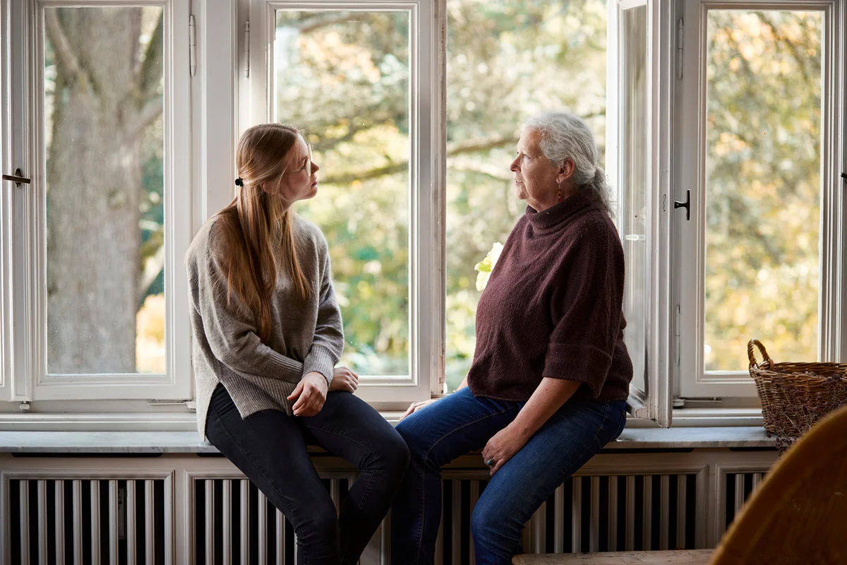 Grandmother and adult granddaughter sitting on windowsill