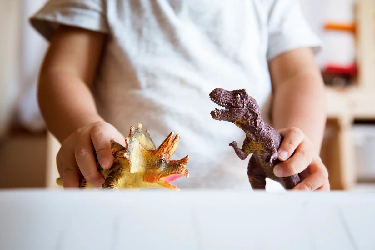 Hands of boy playing with miniature scale dinosaurs
