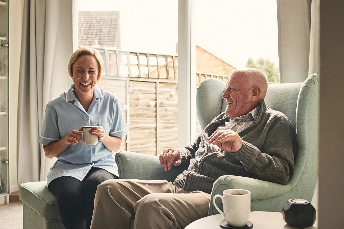 Senior man and female carer enjoying coffee at home