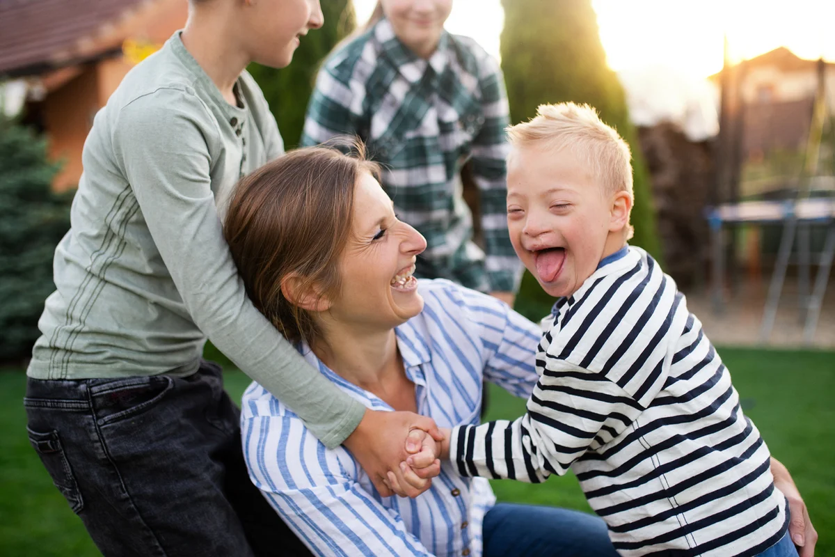Down syndrome boy playing with mother and siblings outdoors in garden