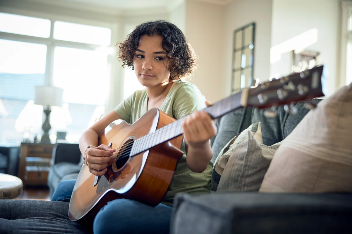 Teenage girl playing guitar on the sofa