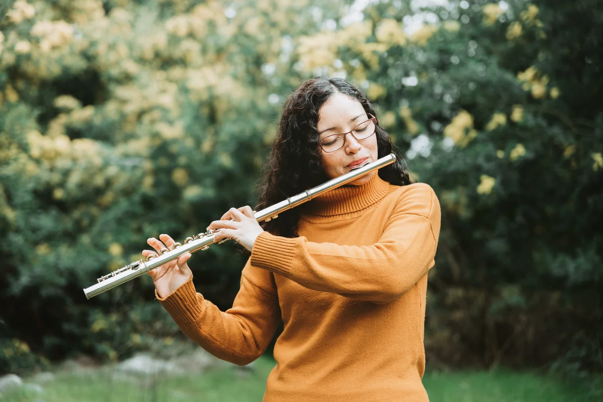 Woman with glasses playing transverse flute outdoors