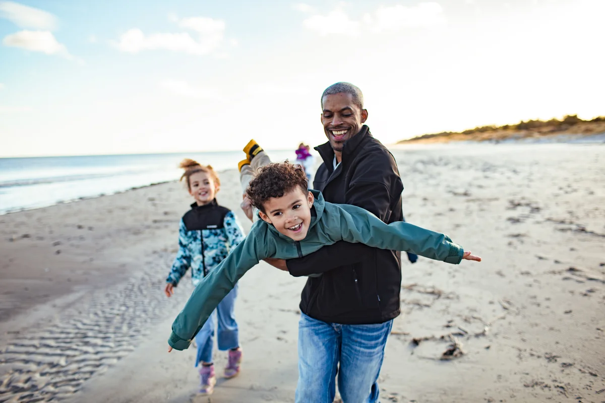 Dad carrying son on beach like an airplane