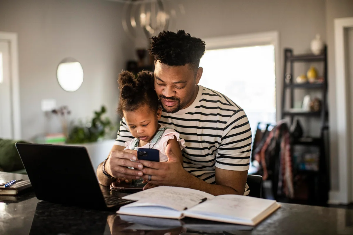 Dad sitting with young daughter, planning vacation on computer and paper