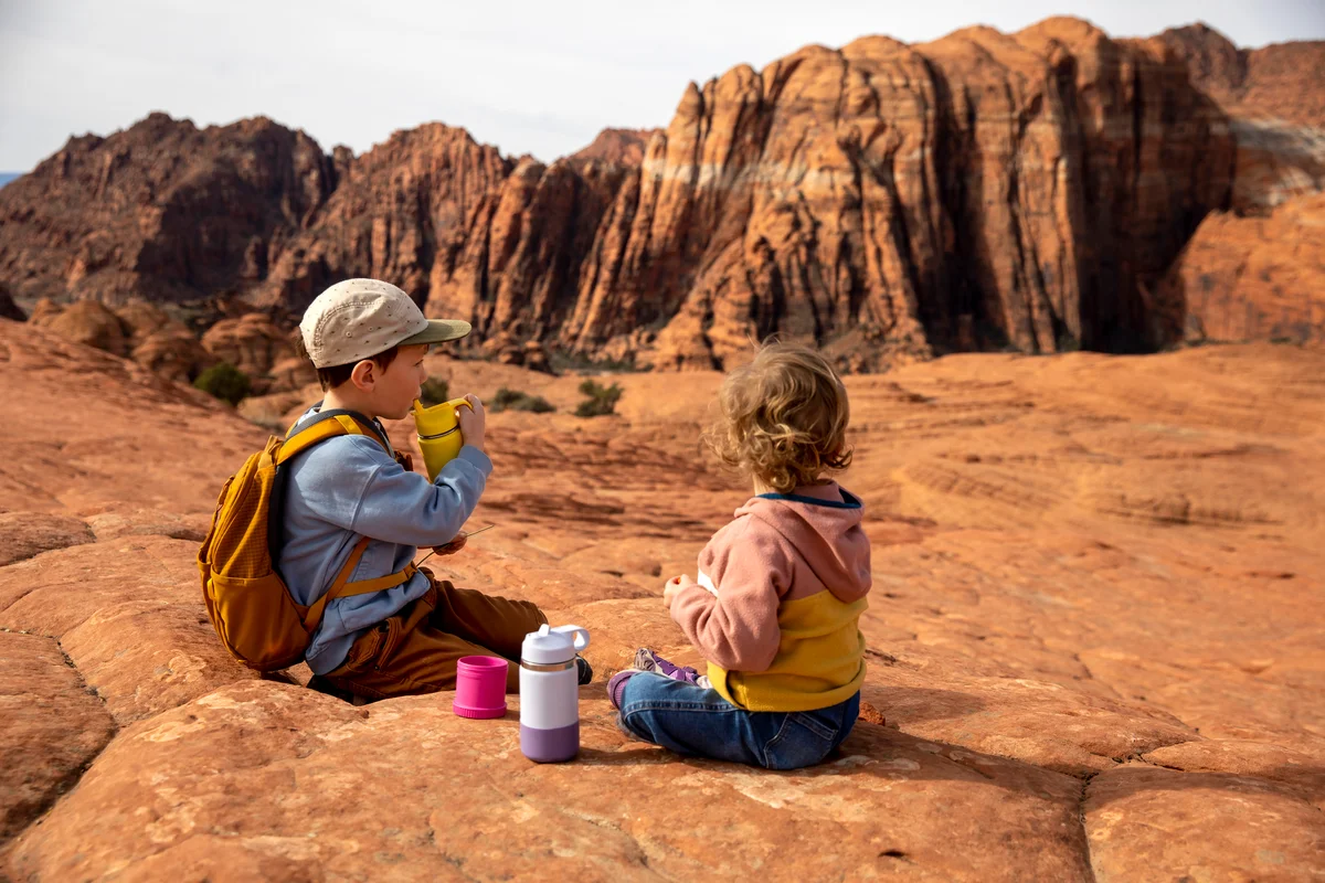 Two kids snacking and drinking water while they rest on a family hike
