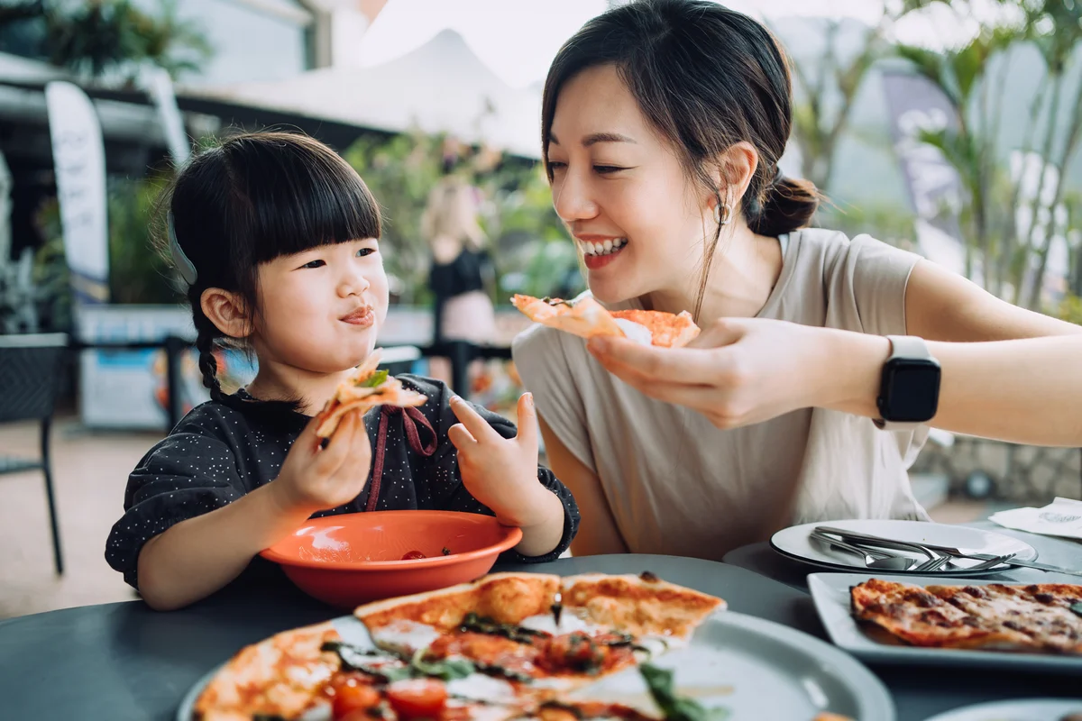 Mom feeding her young daughter pizza