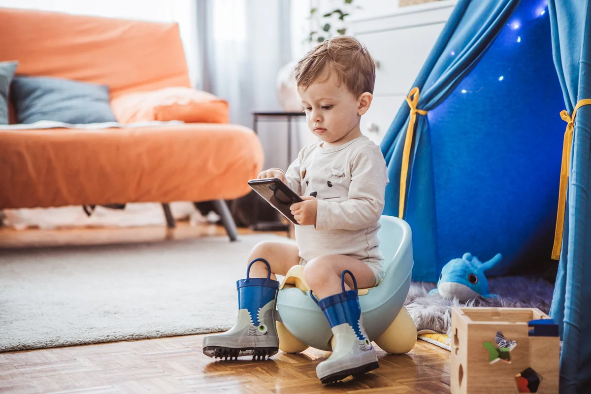 Baby boy in boots sitting on potty and watching cartoons