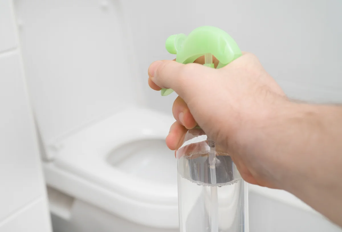 Hand aiming homemade air freshener disinfectant at toilet
