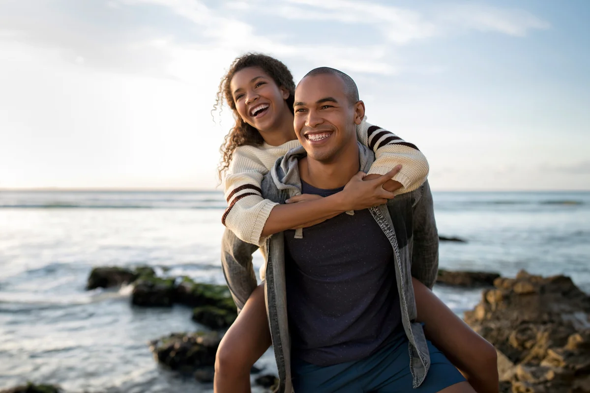 man giving girlfriend a piggyback ride at the coast
