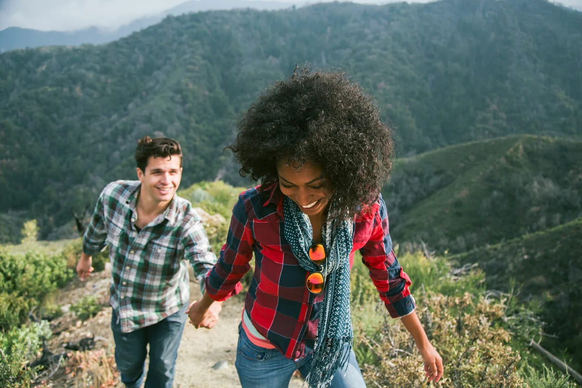 Young woman leading boyfriend up a mountain trail