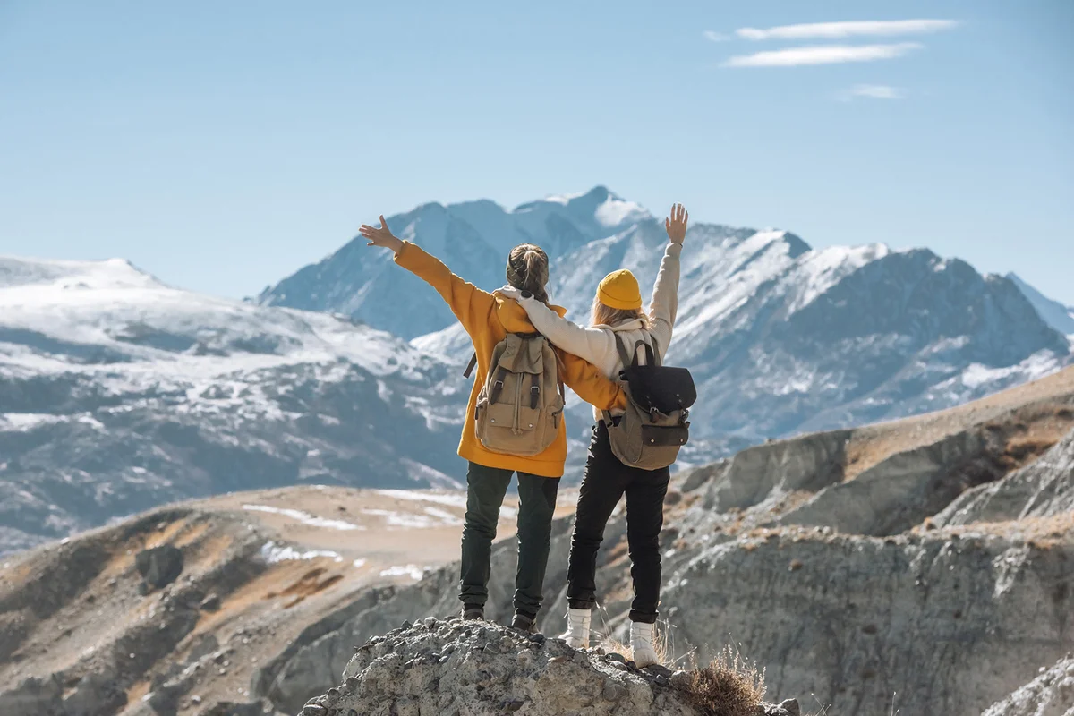 Two women with backpacks together on top of a mountain