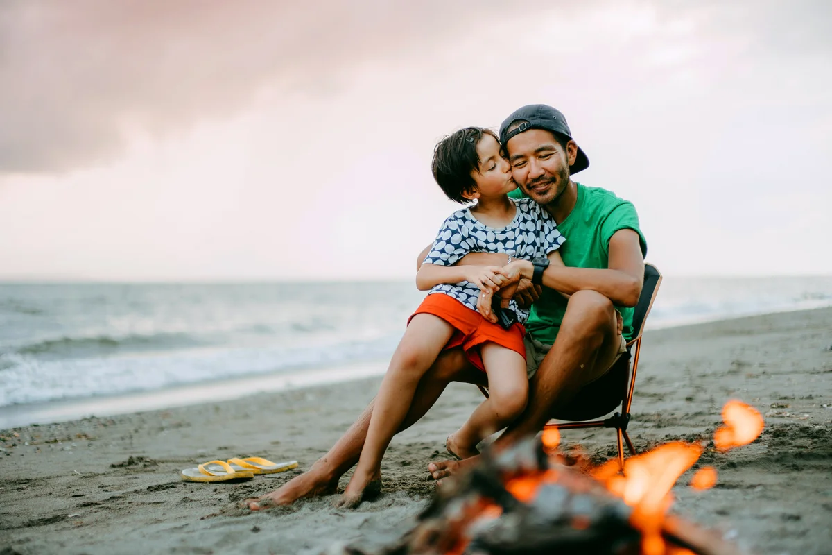 Young girl kissing her father on beach with campfire