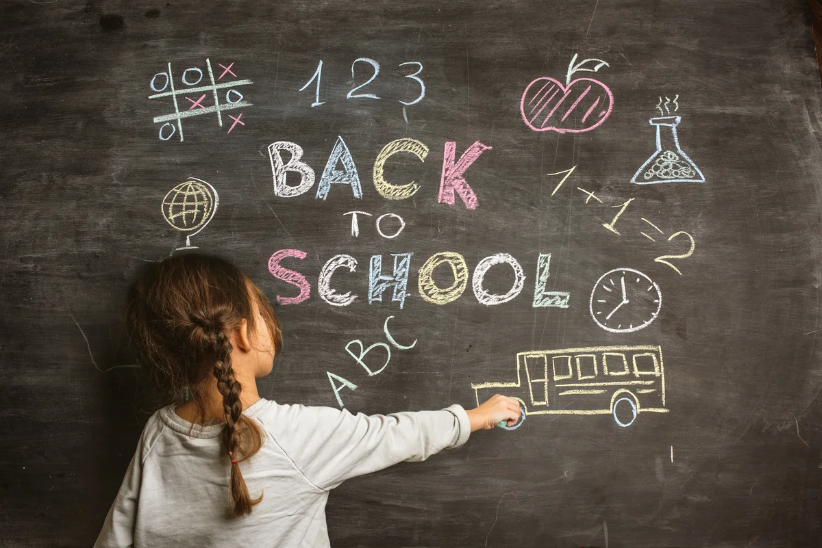 Little girl writing Back to School on blackboard