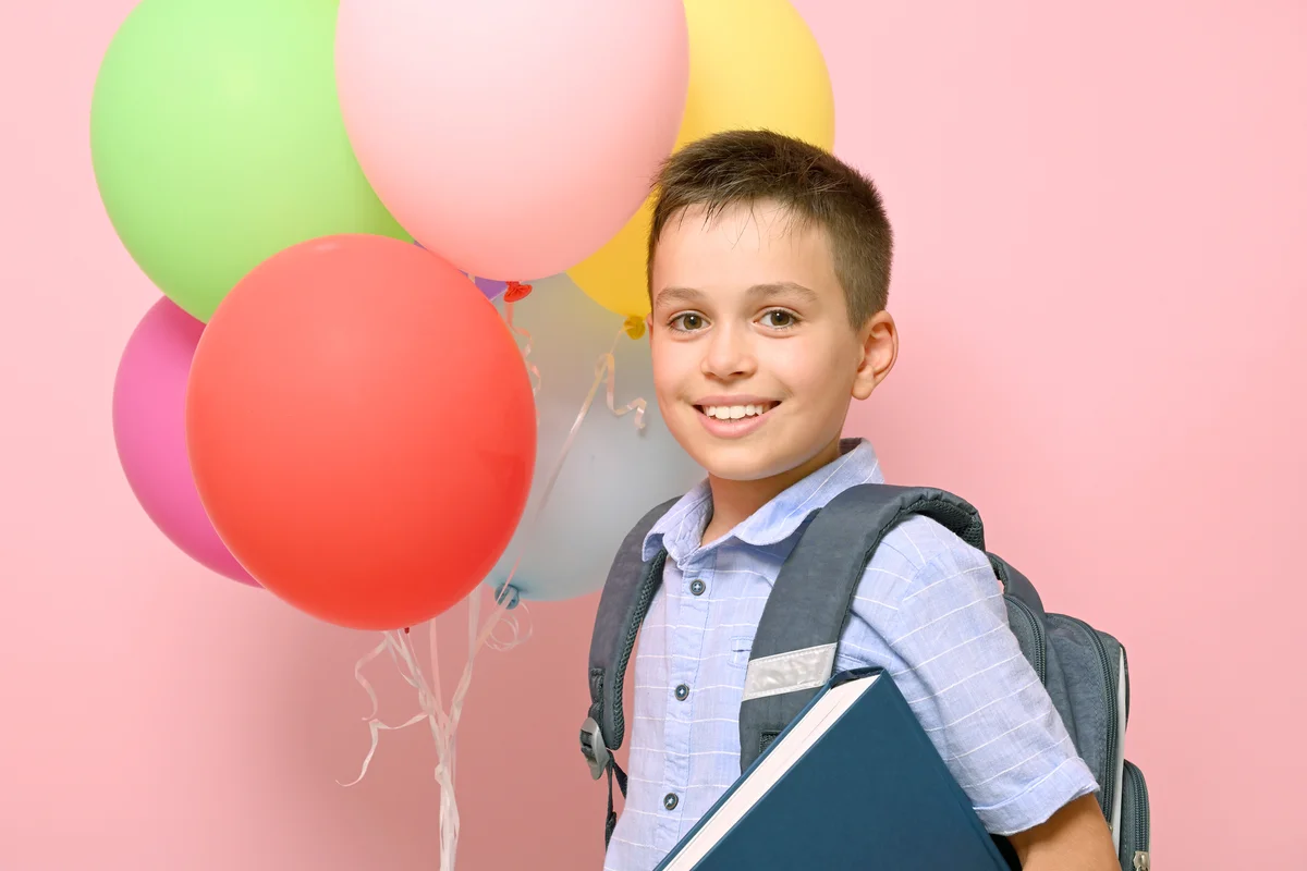 Schoolboy with backpack holding book and multicolored balloons