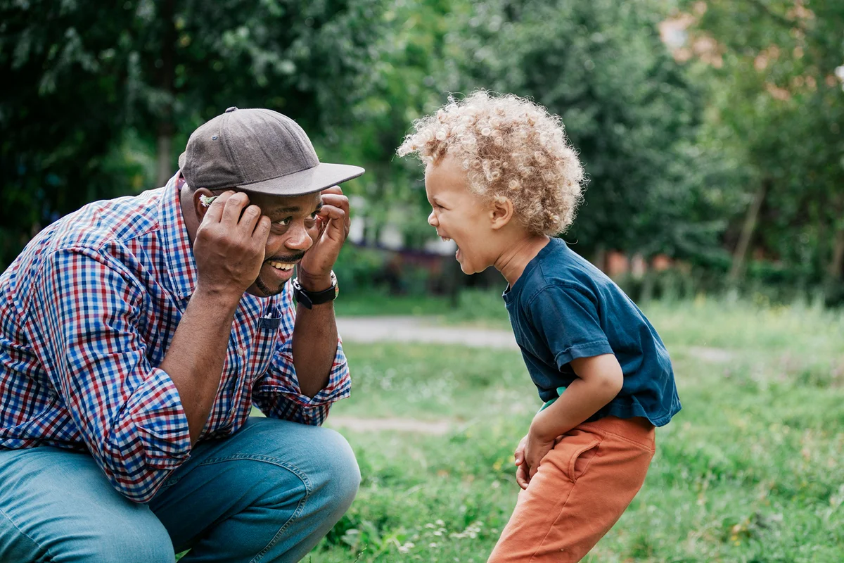 Young Boy Laughing At Playful Grandfather In Park